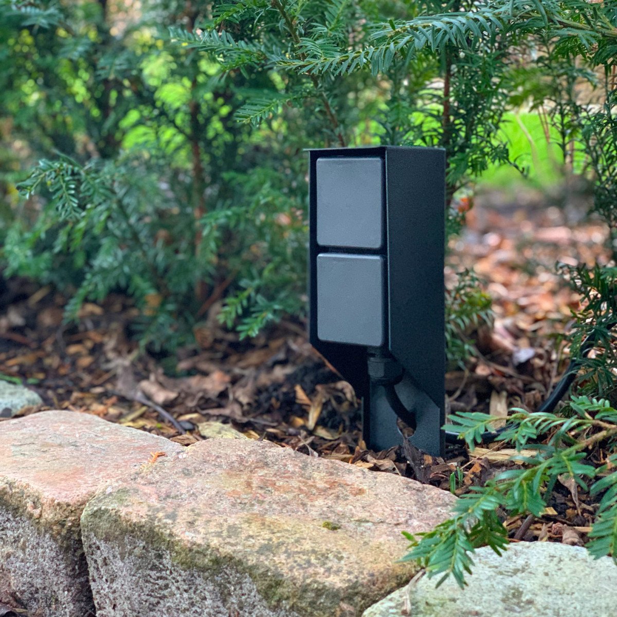 Prise extérieure noire avec piquet pratique et deux points de courant pour éclairage de jardin.